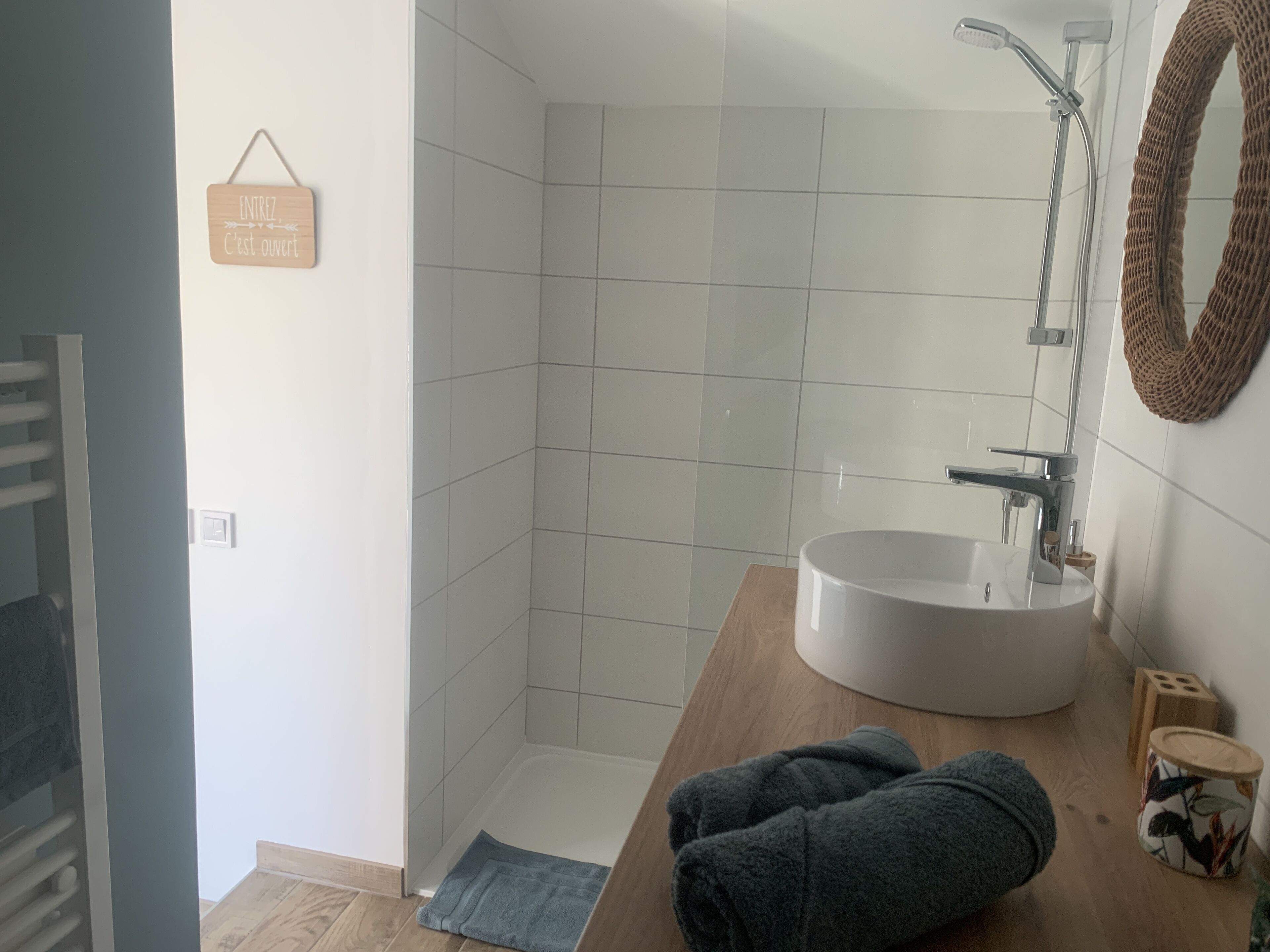 A bathroom with a white sink, a shower, and a towel on the floor.