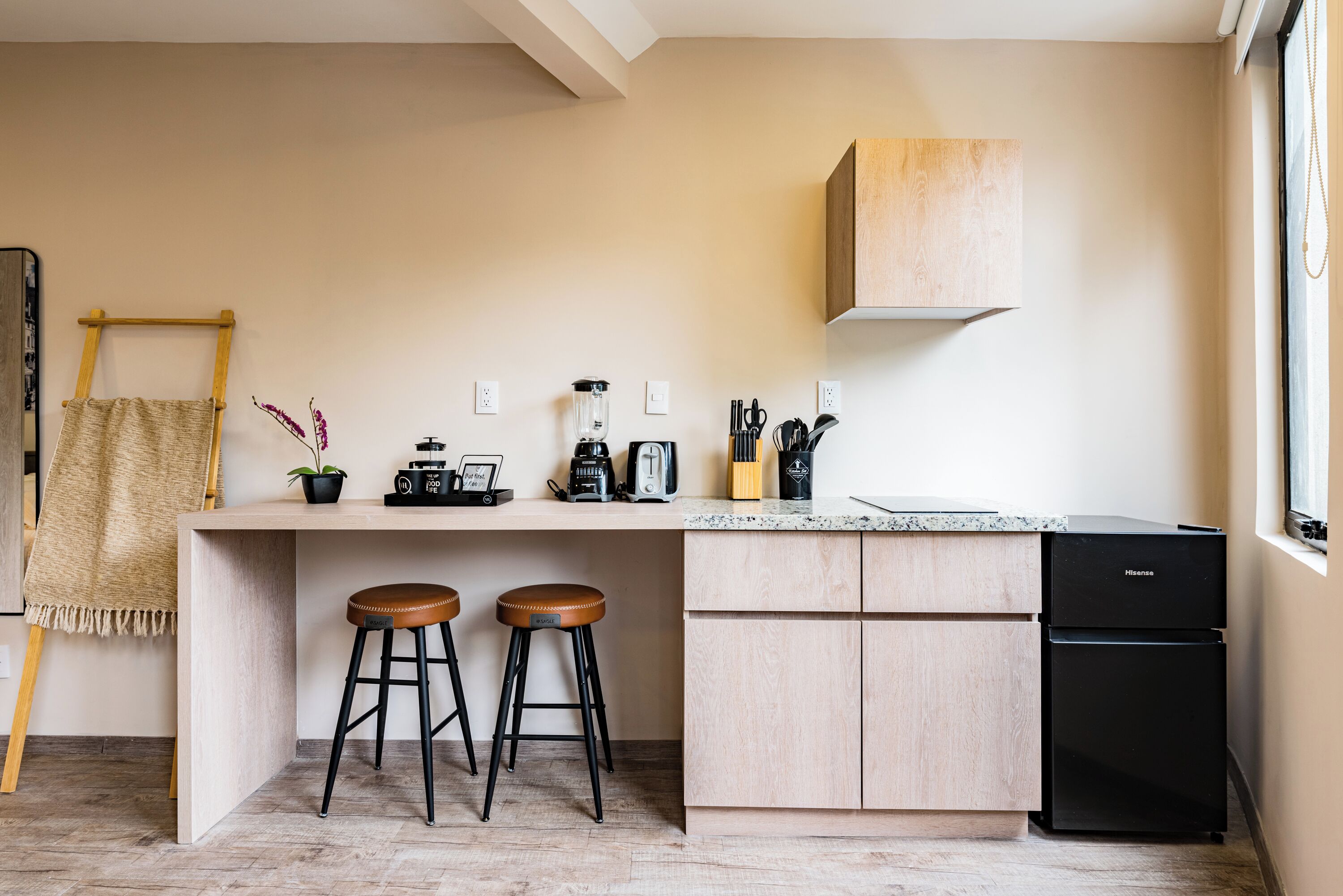 A modern kitchen with a wooden island, two stools, a black refrigerator, and a hanging plant.