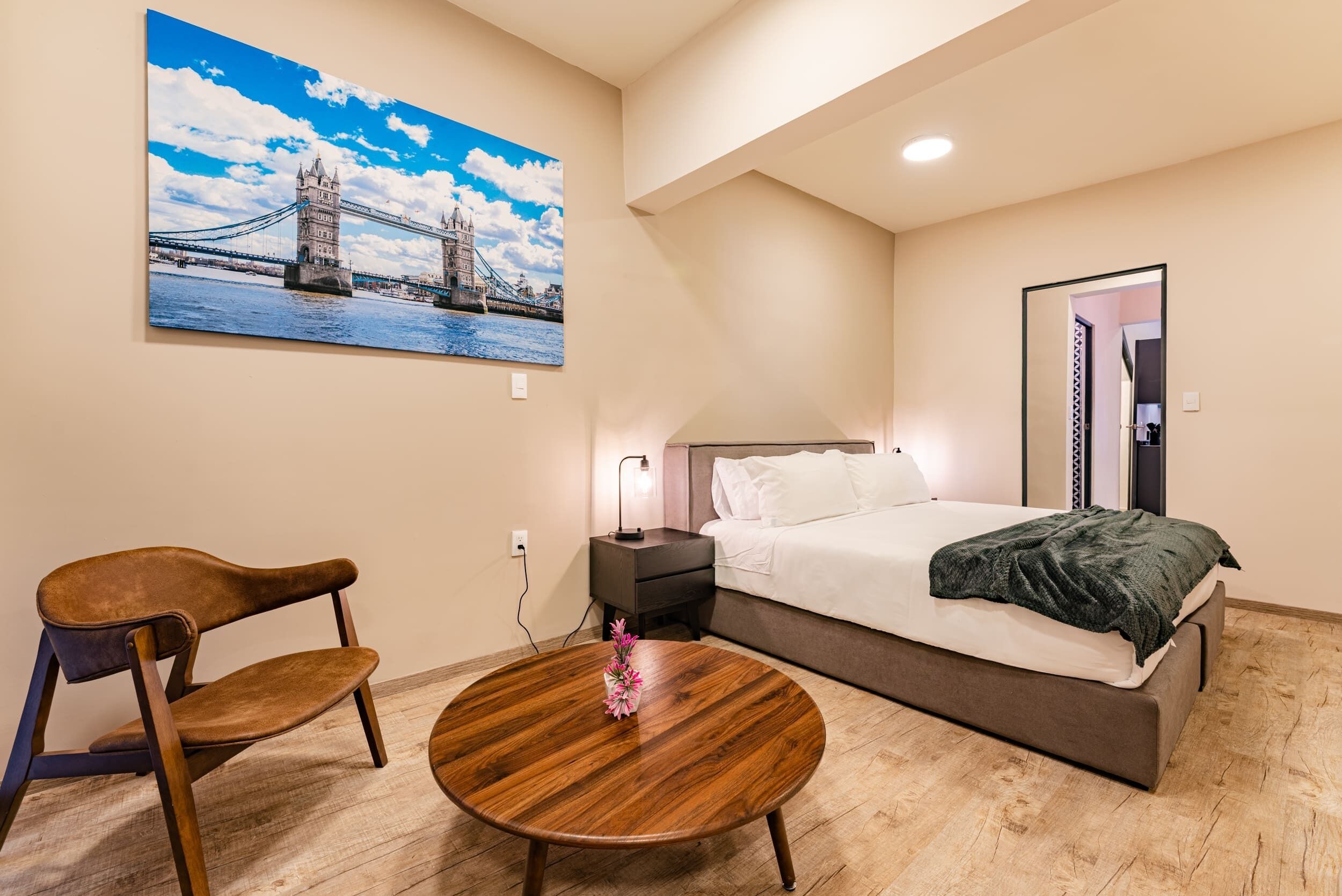 Une chambre à coucher comprenant un lit, une table de chevet, une chaise, une table ronde en bois et un tableau représentant un pont.