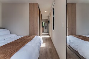 Ein Hotelzimmer mit zwei Betten, Holzboden und einer kleinen Küchenzeile im Hintergrund.