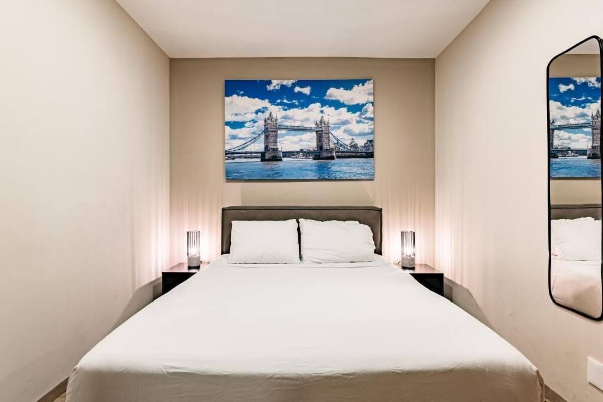 Ein Hotelzimmer mit einem großen Bett, zwei Nachttischen, einem wandmontierten Spiegel und einem Bild von der Tower Bridge.