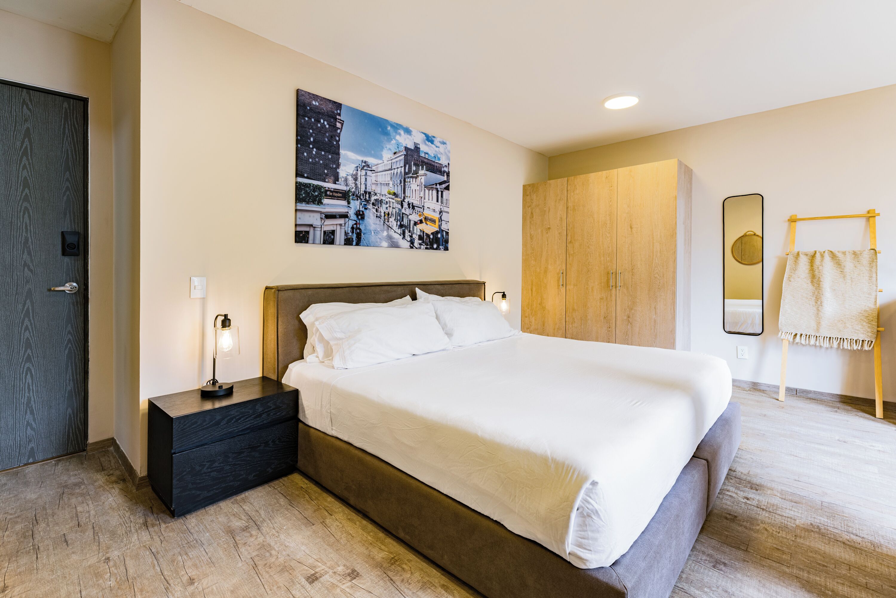 Ein modernes Schlafzimmer mit einem großen Bett, einem Nachttisch, einem Holzschrank, einem Spiegel und einem Stadtbild an der Wand.