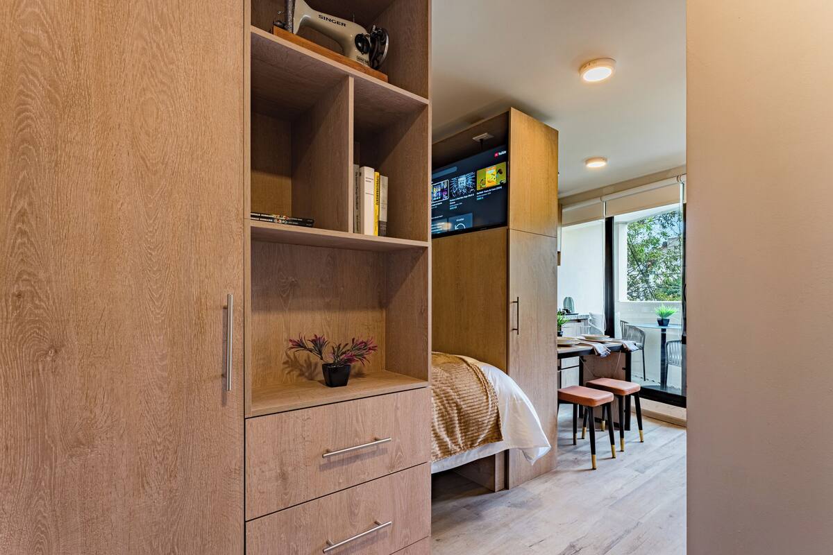 Ein modernes Schlafzimmer mit Holzschrank, Bett und Schreibtisch, mit Blick ins Freie.