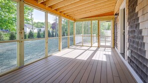 A covered porch with wooden beams, large windows, and a view of a residential area. - Unique Scituate Vacation Rental on Herring River! (Scituate)