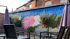 Outdoor seating with metal chairs and umbrellas, a mural on a brick wall, and a paved patio. - Oakham hotel (Oakham)