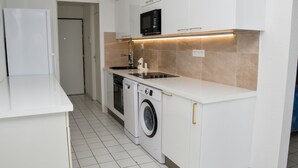 Una cocina compacta con muebles blancos, un microondas integrado, una lavadora y un lavamanos.