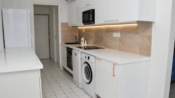 A compact kitchen with white cabinetry, a built-in microwave, a washing machine, and a sink.