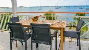 Una mesa de madera con cuatro sillas en un balcón con vista a un puerto deportivo lleno de veleros.