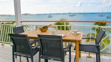 A wooden table with four chairs on a balcony overlooking a marina with sailboats.