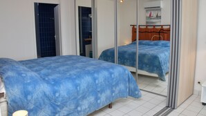 Un dormitorio con dos camas, un ventanal corredero y un pequeño estante con adornos.