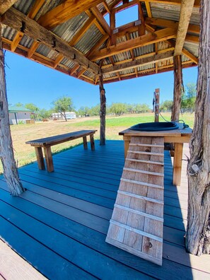 A wooden deck with a bench and a table, surrounded by trees and a clear sky. - The Avion ~ Glamping in Spicewood TX Hill Country at Green Acres (Spicewood)