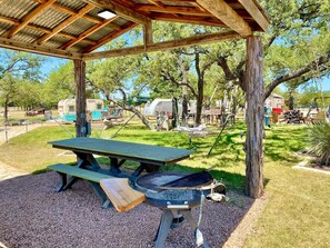 A covered picnic area with a grill, picnic table, and surrounding trees. - The Avion ~ Glamping in Spicewood TX Hill Country at Green Acres (Spicewood)