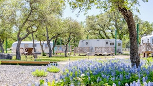 Un terrain de camping équipé d’emplacements pour camping-cars, de tables de pique-nique et d’un champ de fleurs bleues.