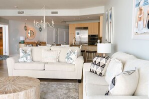A modern living room with a beige sofa, a round coffee table, and a kitchen in the background.