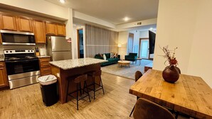 A modern kitchen with stainless steel appliances, a wooden dining table, and a seating area with a sofa and chairs. - 2 bed 2 bath apartment in Castle (Grandville)