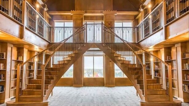 A grand library with a central staircase flanked by bookshelves, leading to a large window at the top. - 2 bed 2 bath apartment in Castle (Grandville)