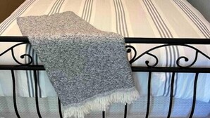 Een bed met gestreepte lakens, een rond kussen met tekst en een grijze plaid.