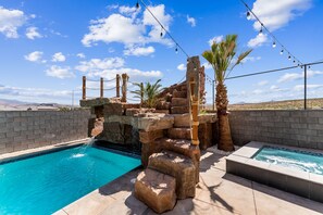 A pool area with a rock waterfall feature, palm trees, and string lights.