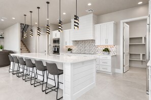 A modern kitchen with a central island, bar stools, white cabinetry, and pendant lighting.