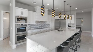 A modern kitchen with white cabinetry, stainless steel appliances, and a large island with bar stools. - Sand Hollow Aquatic Adventure (Hurricane)
