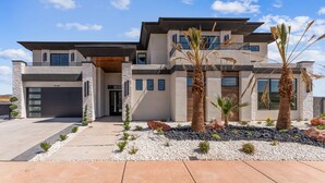 A modern two-story house with a garage, stone facade, and a landscaped front yard with palm trees and rocks. - Sand Hollow Aquatic Adventure (Hurricane)