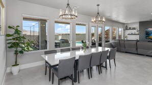 A modern kitchen with a large island, a dining area with a white table and chairs, and a view of the outdoors through large windows. - Sand Hollow Aquatic Adventure (Hurricane)