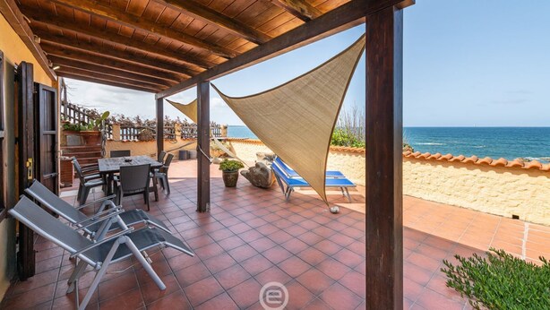 Une terrasse couverte avec des sièges d’extérieur, une table et une vue sur la plage et l’océan.