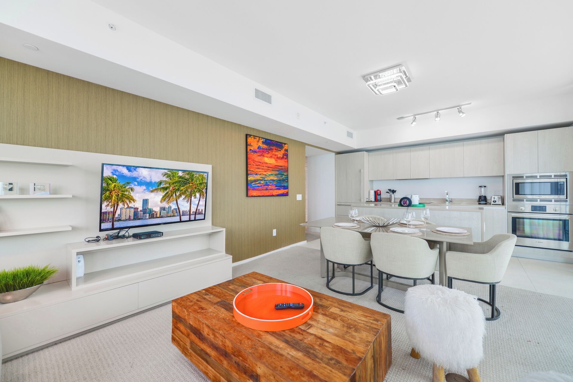 A modern living room with a flat-screen TV, a dining area with a table set for two, and a kitchen with contemporary appliances.
