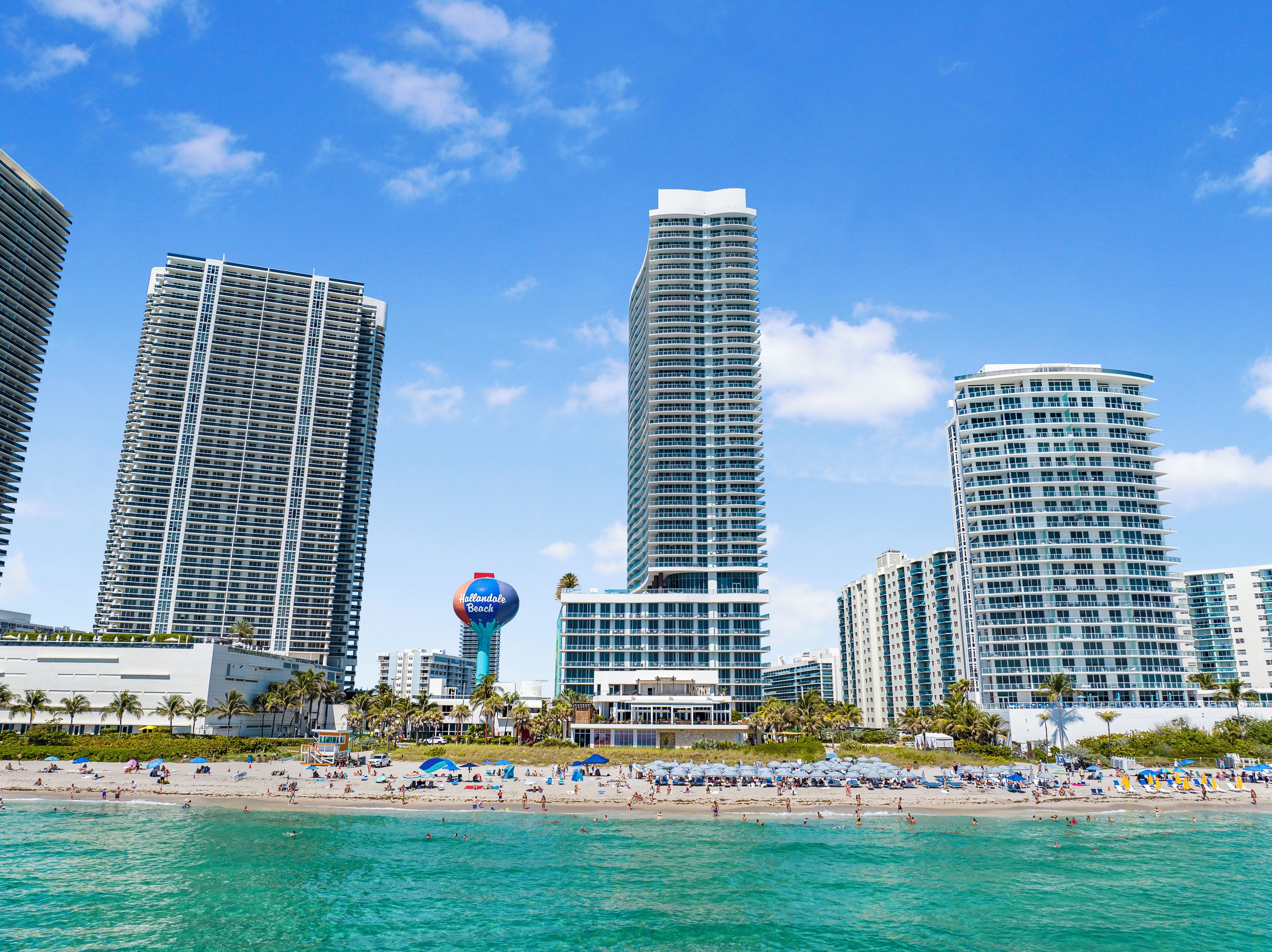 Un hotel frente a la playa con edificios altos, una playa y un cielo azul despejado.