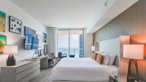 A modern hotel room with a large bed, a desk, a chair, and a view of the city skyline. - 4111s Hollywood - Steps to the Sand - We Host (Hollywood)