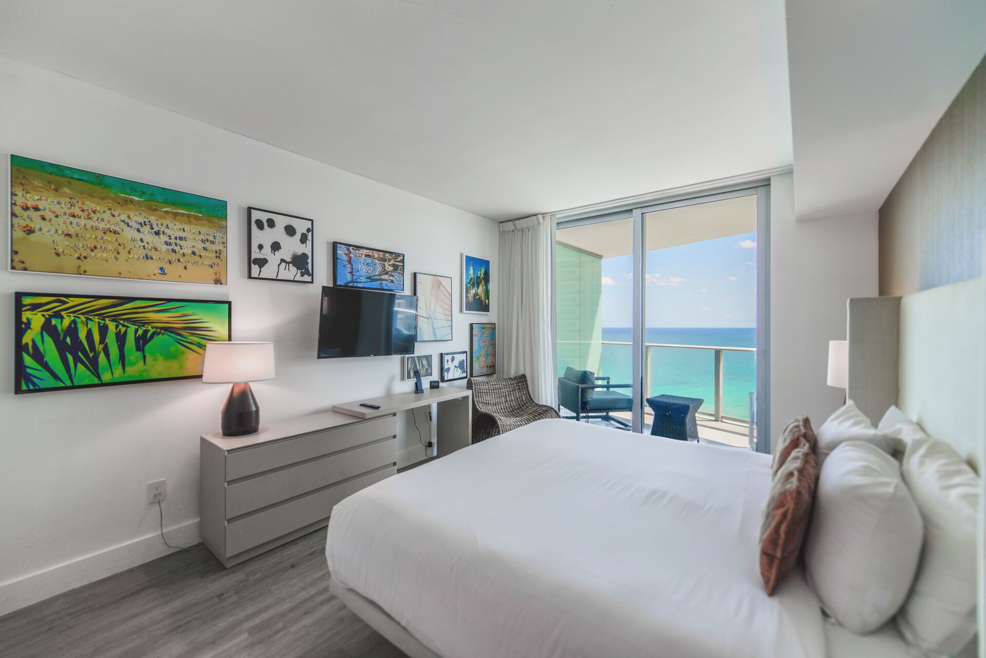 Quarto de hotel com cama, escrivaninha, televisão e obras de arte nas paredes.