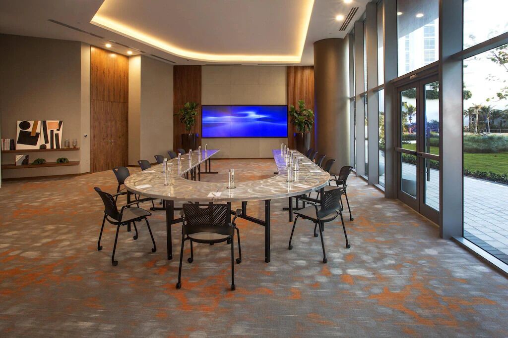 A conference room with a large oval table, black chairs, and a flat-screen TV on the wall.