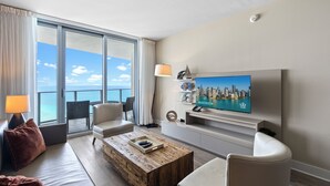 A modern living room with a large TV, comfortable seating, a coffee table, and a balcony with a city view. - 4111s Hollywood - Steps to the Sand - We Host (Hollywood)