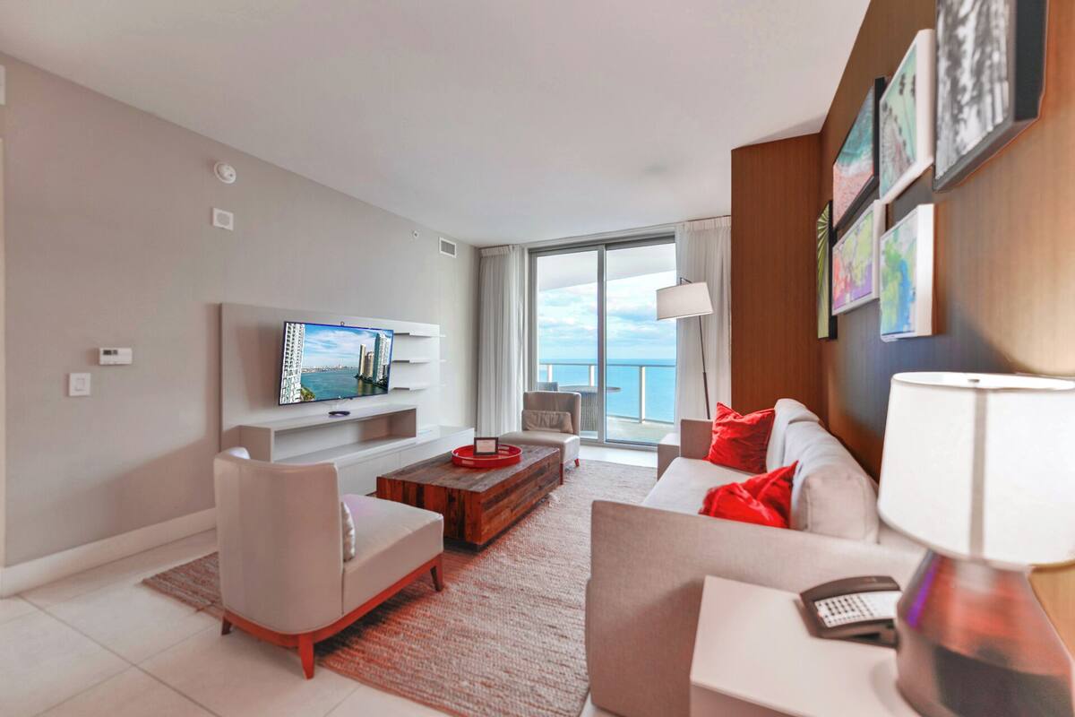 Een moderne woonkamer met een flatscreen televisie, een bank, een salontafel en een balkon met uitzicht op zee.