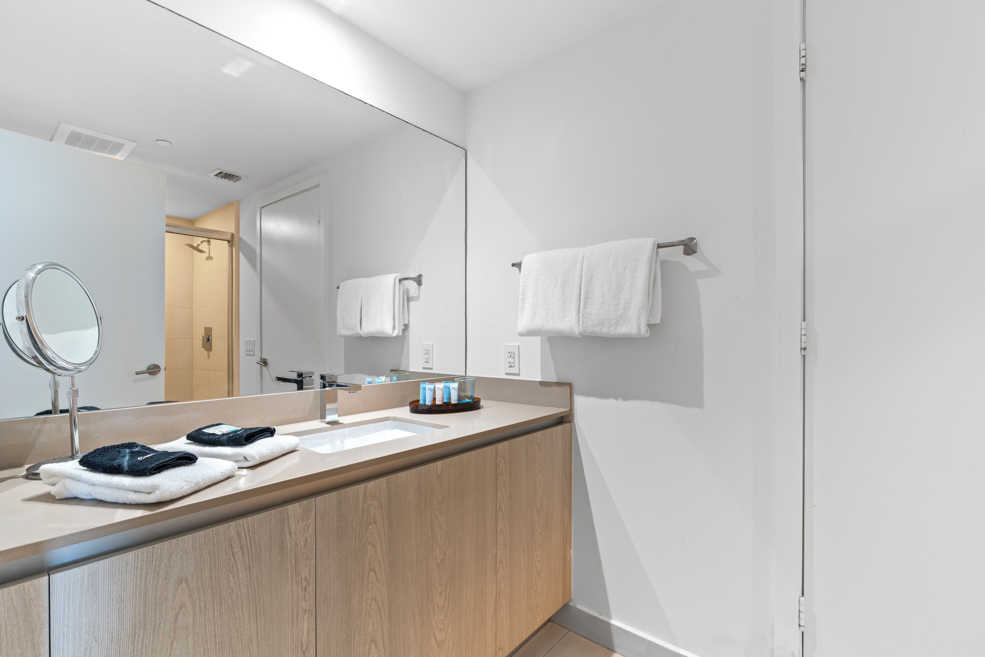 A modern bathroom with a large mirror, two sinks, wooden cabinets, and a towel rack.