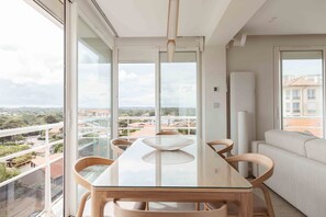 Een moderne eetruimte met een glazen tafel en houten stoelen, grote ramen met uitzicht op de stad.