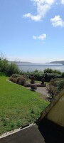 A grassy area with a pathway leading to a body of water, surrounded by greenery and a clear sky.