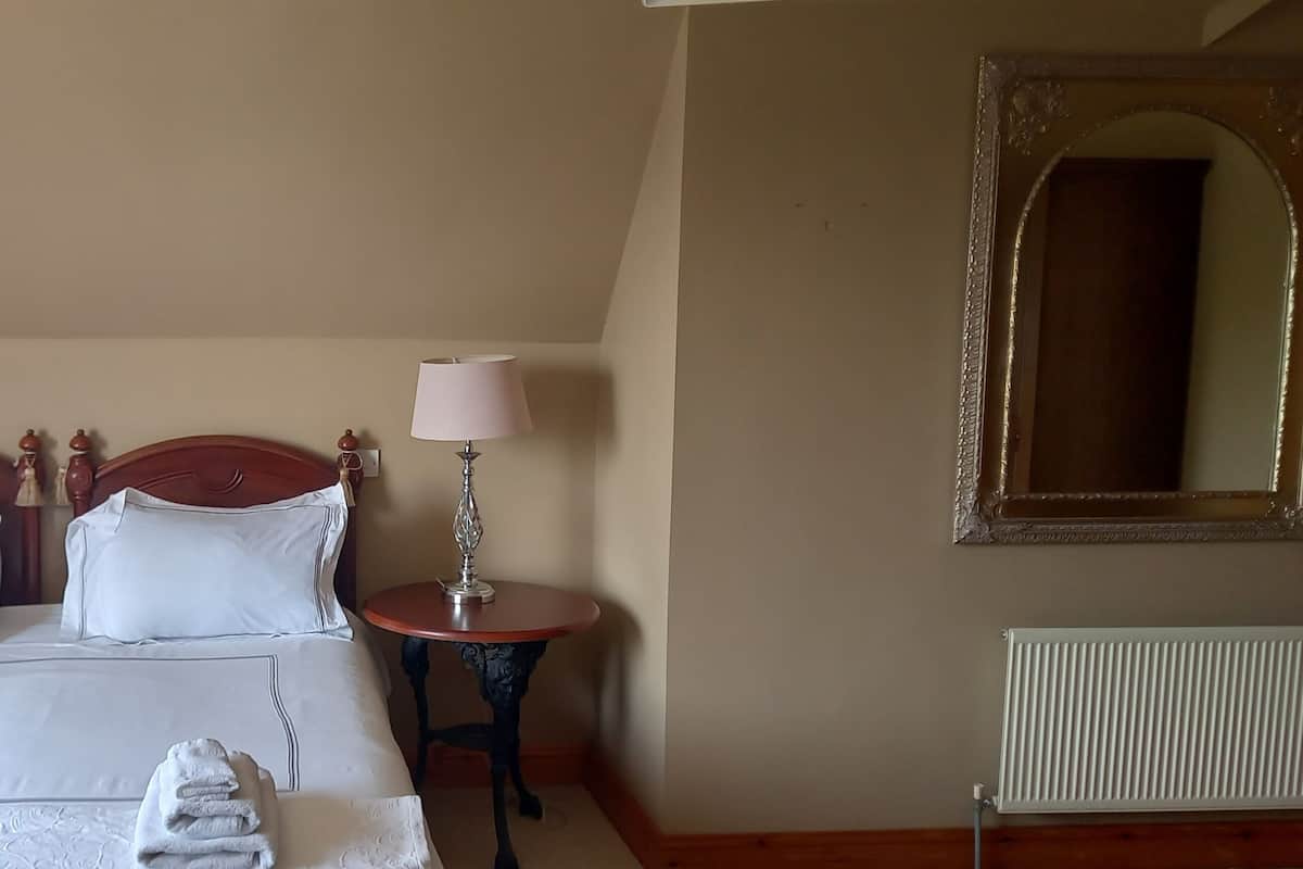 A neatly made bed with white linens and pillows, two bedside tables with lamps, a mirror on the wall, and a radiator.
