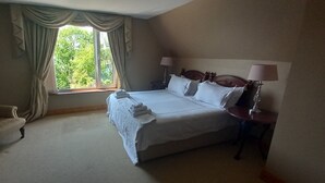 A hotel room with a large bed, a chair, a nightstand with a lamp, and a window with curtains. - Ardsallagh Lodge (Tinnabinna)