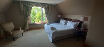 A hotel room with a large bed, a chair, a nightstand with a lamp, and a window with curtains.