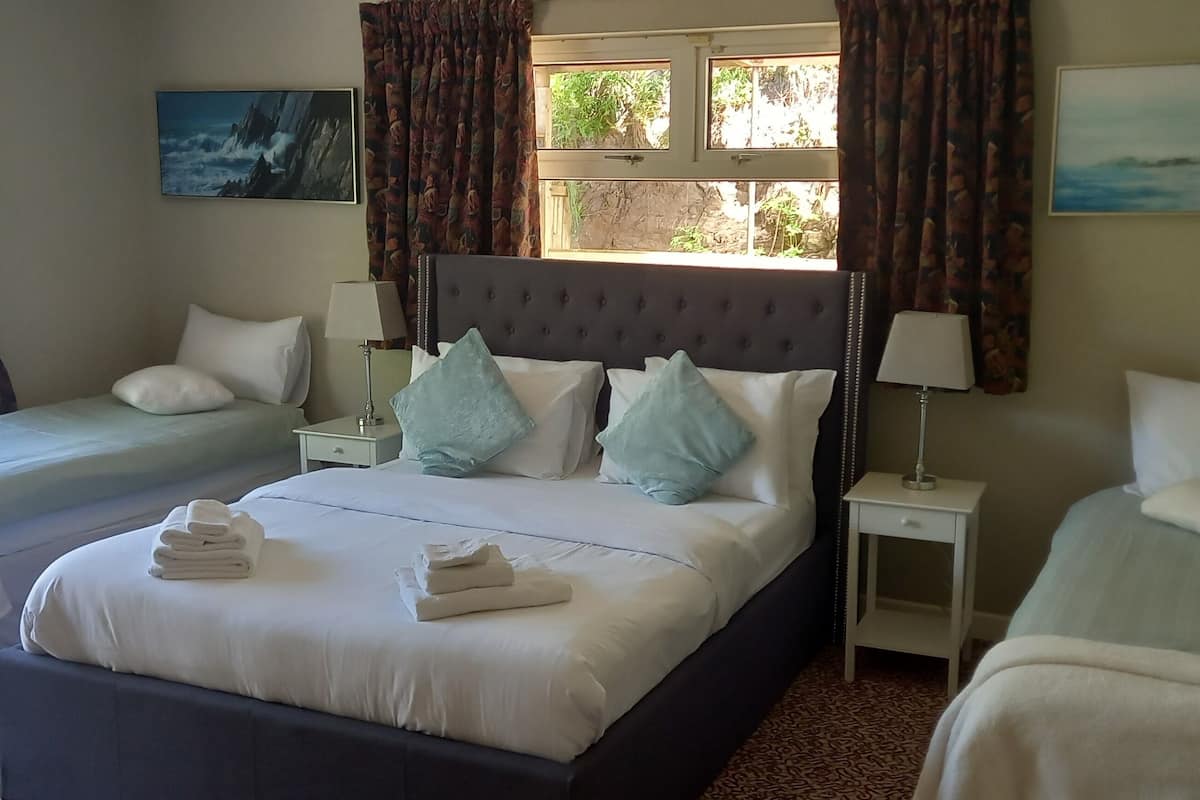A hotel room with two single beds, a larger bed, and a nightstand with a lamp.