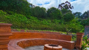 A circular outdoor seating area with a fire pit, surrounded by brick walls and greenery. - Confort Arenal (La Fortuna)