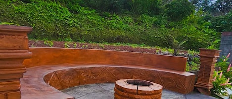 A circular outdoor seating area with a fire pit, surrounded by brick walls and greenery.