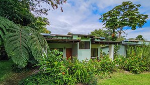 A house with a green roof, surrounded by lush greenery and a clear sky. - Confort Arenal (La Fortuna)