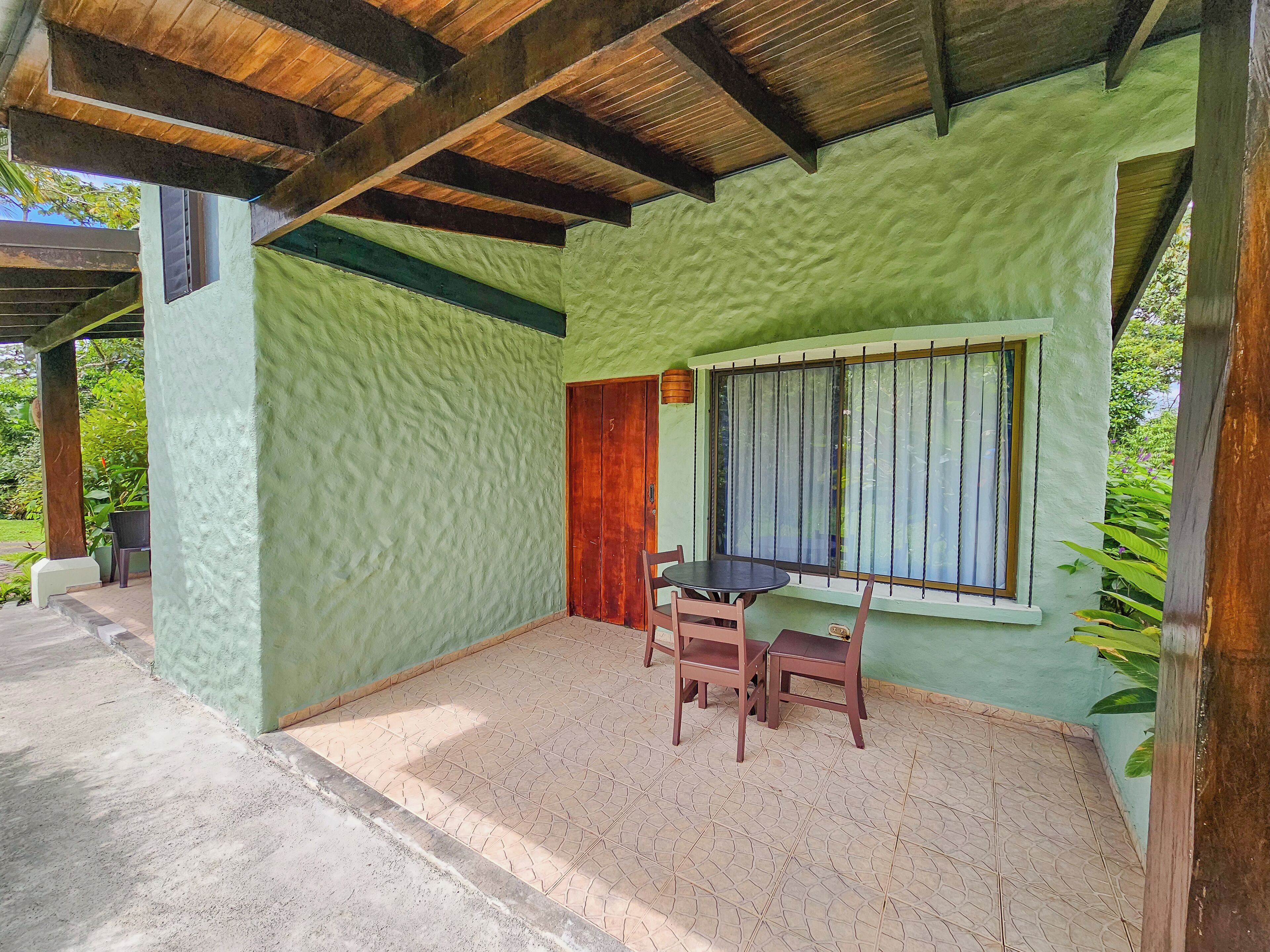 A covered outdoor area with a green wall, a wooden door, and a window with bars.