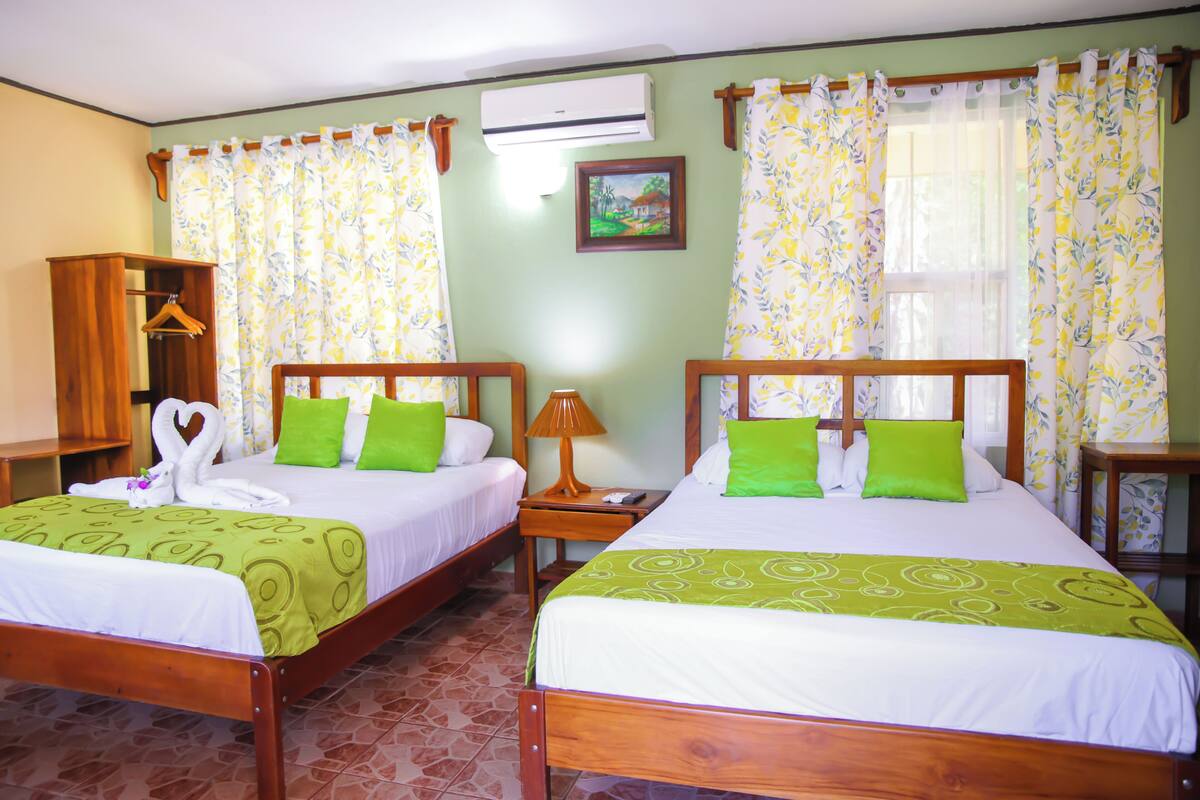 A hotel room with two beds, a wooden wardrobe, an air conditioner, and a framed picture on the wall.