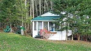 A small, white wooden structure with a green roof, surrounded by trees and a grassy area. - Cozy Cottage, Dog Friendly, Close to beach, Natural Wood, Waterfall on site (Barton)