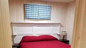 A bedroom with a red bedspread, a checkered window blind, a bedside lamp, and a wooden floor. - Cozy Cottage, Dog Friendly, Close to beach, Natural Wood, Waterfall on site (Barton)