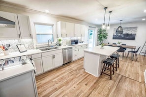 Uma cozinha moderna com armários brancos, piso de madeira, uma ilha central com banquetas e um espaço de refeições com mesa e cadeiras.