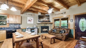 A wooden interior with a dining table set, a fireplace, a leather couch, and a door with a stained glass window. - Spacious Family Fun Cabin with Slide, Hot Tub, Games & Great Location! Pets ok (Pigeon Forge)